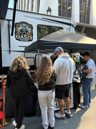 Four people at a mobile cigar lounge booth under a black canopy beside a white trailer on a downtown city street, outdoor event vibe