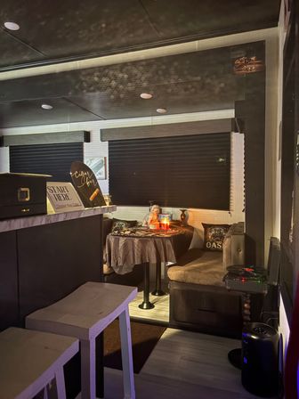 Cozy candlelit RV dining nook with round table, plush bench seating, small bar counter and two stools under dark window shades.