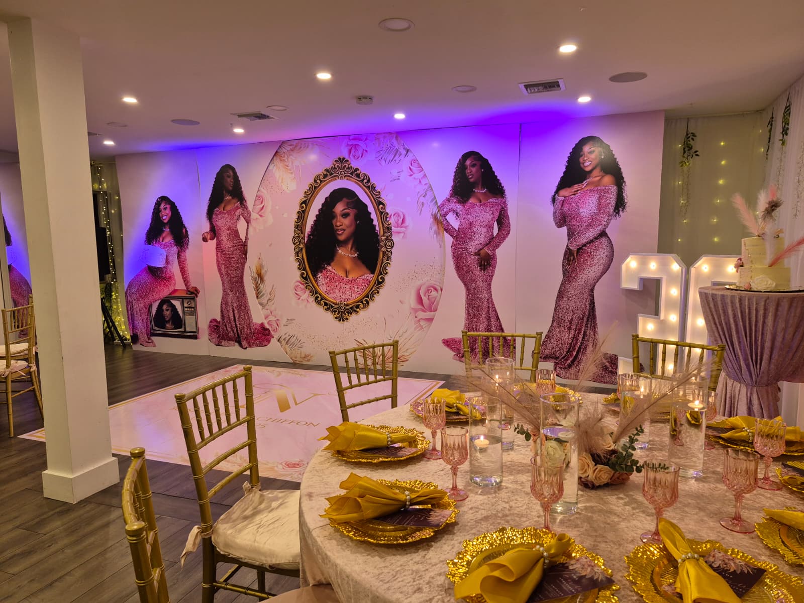 Glamorous indoor event hall set for a pink-and-gold 30th birthday celebration: round tables with gold chargers, yellow napkins, pink glassware and floral centerpieces, gold Chiavari chairs, dance floor, large life‑size portrait backdrop under purple uplighting and illuminated '30' marquee.