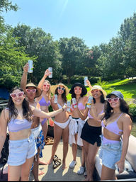 Sunny lake boat party: group of friends in lavender swimsuits and heart-shaped sunglasses toasting with canned drinks on a dock surrounded by green trees
