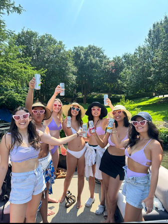 Sunny lake boat party: group of friends in lavender swimsuits and heart-shaped sunglasses toasting with canned drinks on a dock surrounded by green trees