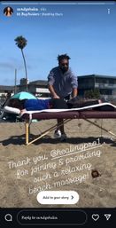 Outdoor beach massage on a portable table — a therapist stretches a client's leg on a sunny sandy shore with a palm tree and oceanfront buildings in the background, relaxing seaside wellness scene.