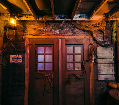 Dimly lit rustic boathouse interior with weathered double wooden doors and frosted panes, warm lantern light, hanging fishing nets, ropes, buoys and maritime decor