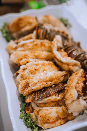 Close-up of mouthwatering butter-basted grilled lobster tails seasoned with paprika, arranged on a white platter garnished with microgreens — seafood platter