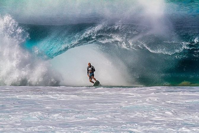 Surfer carving inside a massive turquoise barrel wave at a powerful reef break with foamy white water in the foreground.