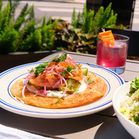 Outdoor patio brunch: crispy flatbread topped with smoked salmon, pickled red onion, cucumber, dill and cream, paired with a pink cocktail