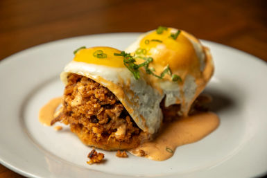 Brunch plate with two sunny-side-up eggs atop a savory seasoned crumb topping, drizzled with creamy orange sauce and garnished with chopped green onions on a white plate