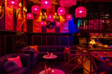 Urban cocktail lounge interior with velvet sofas, marble tables and pink fringe pendant lamps casting a moody vintage‑glam glow over a glowing bar.
