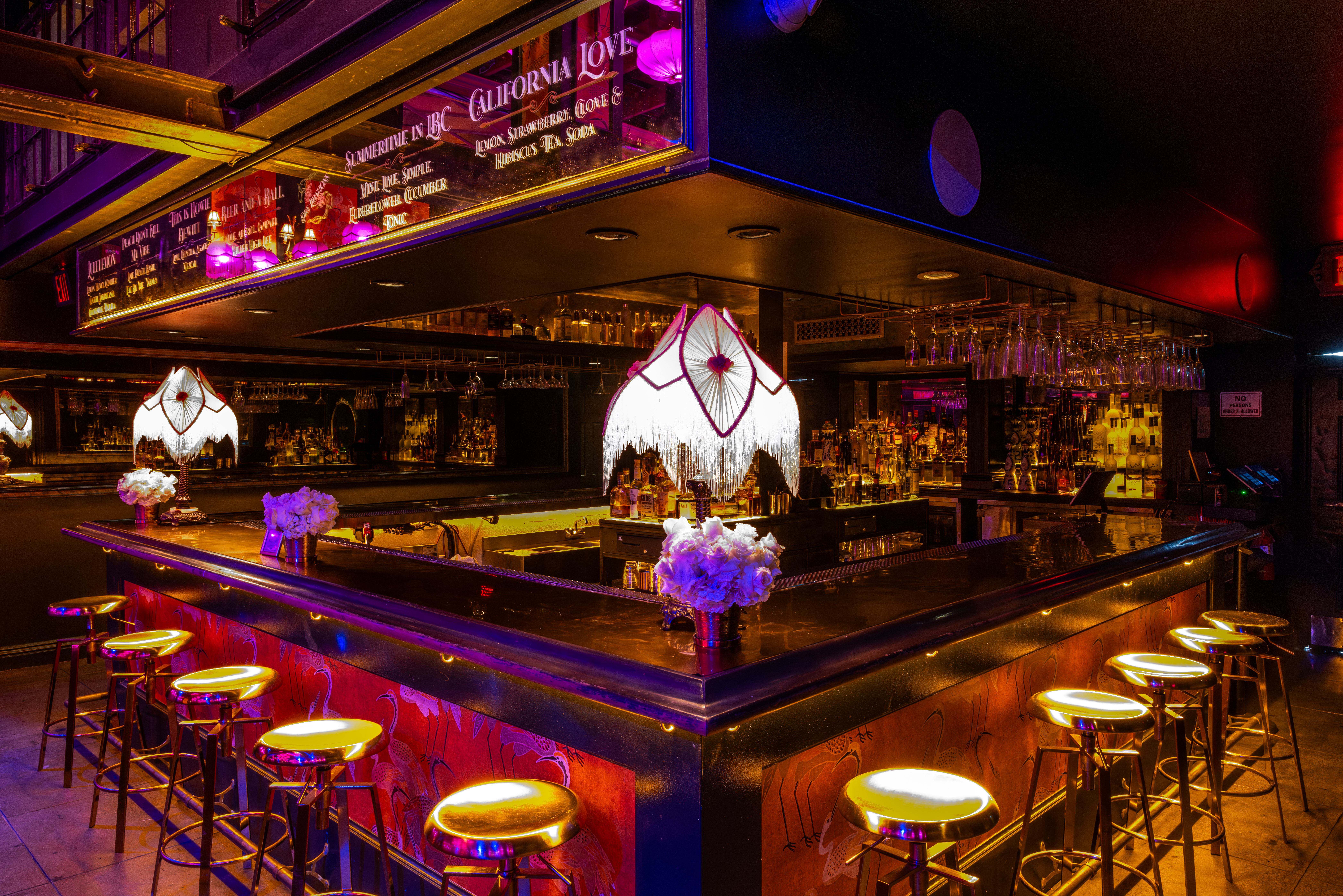 Neon-lit urban cocktail bar interior with a U-shaped polished bar, fringe vintage lamps, brass stools, mirrored shelves of bottles and hanging glassware, moody late-night lounge vibe.