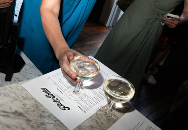 Hand placing two coupe glasses of sparkling wine on a marble bar counter over printed menus at an indoor bar event