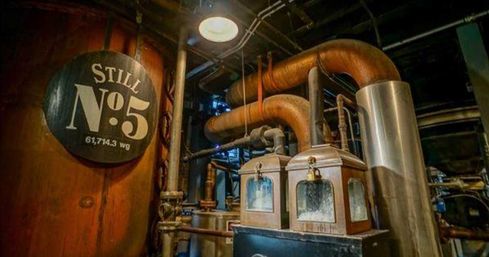 Distillery interior featuring large copper stills and curved copper piping, brass fixtures and glass-view housings, plus a round sign reading 'Still No.5'.
