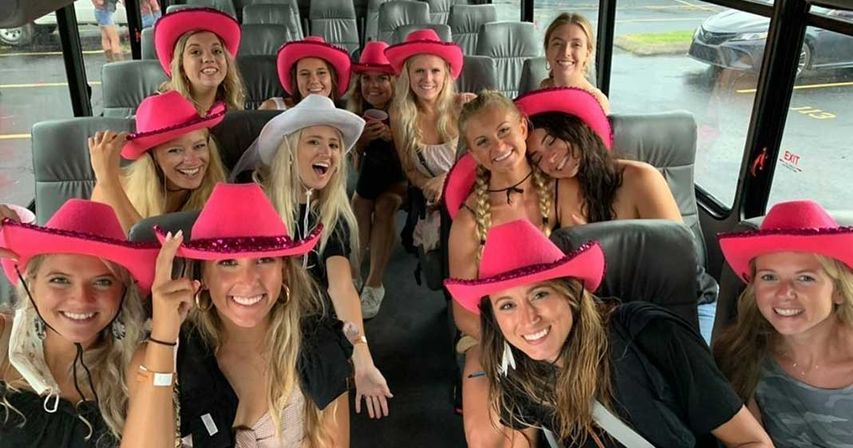 Cheerful group of young women wearing pink cowboy hats, smiling and posing together inside a party bus for a girls' night out