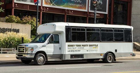 White party shuttle bus with tinted windows parked on a downtown street in front of a museum, advertising hop-on hop-off nightlife tours