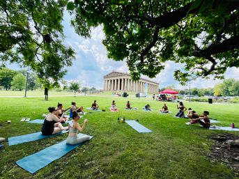 Outdoor yoga group on mats beneath shady trees on the lawn in front of the Parthenon replica at Centennial Park, Nashville