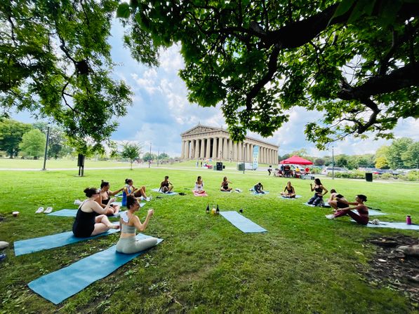 Outdoor yoga group on mats beneath shady trees on the lawn in front of the Parthenon replica at Centennial Park, Nashville