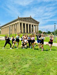 Outdoor yoga group striking tree and prayer poses on the green lawn in front of the Parthenon replica at Centennial Park, Nashville, under a bright blue sky