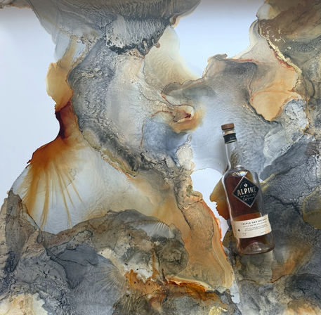 Flat-lay of a glass whiskey bottle with amber liquid and cork resting on an abstract marbled background in gray, gold, rust and white swirls.