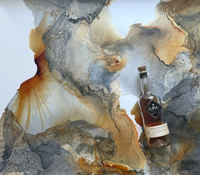 Flat-lay of a glass whiskey bottle with amber liquid and cork resting on an abstract marbled background in gray, gold, rust and white swirls.