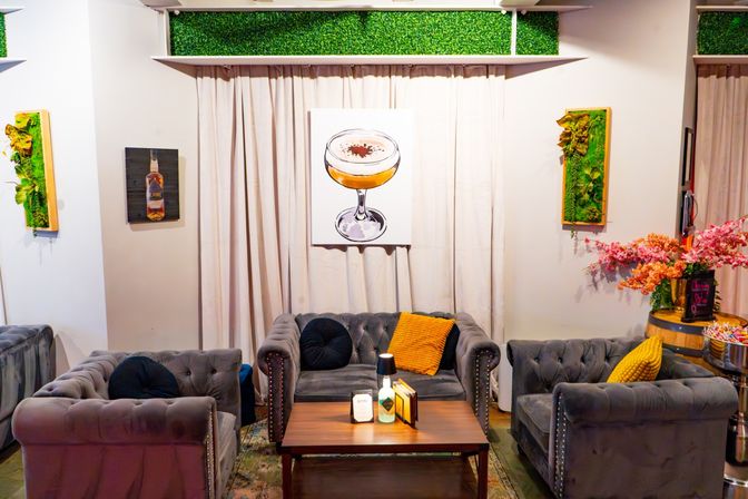 Cozy modern lounge interior with gray tufted velvet sofas around a wooden coffee table, cocktail painting, vertical greenery and pink floral arrangement
