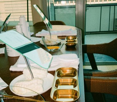 Sunlit balcony manicure station on wooden table with hand mirrors, gold trays, bowls, cotton towels and yellow nail tools, city high-rise view