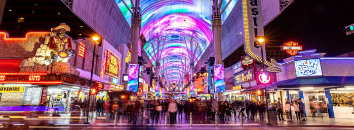 Vibrant neon-lit downtown Las Vegas pedestrian street under a swirling LED canopy at night, bustling crowds and colorful signs blurred by motion