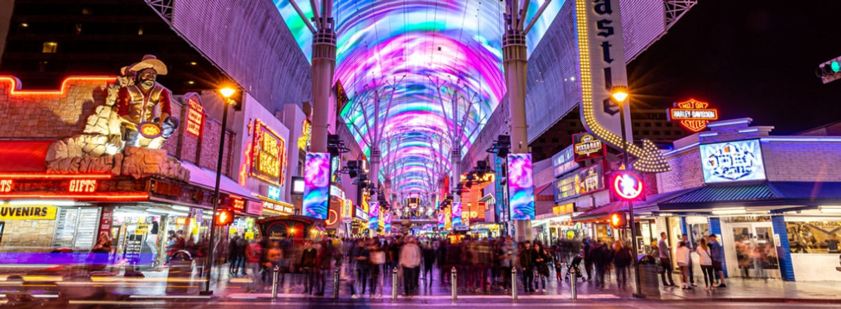 Vibrant neon-lit downtown Las Vegas pedestrian street under a swirling LED canopy at night, bustling crowds and colorful signs blurred by motion
