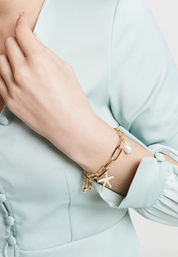 Close-up of a wrist wearing a gold link charm bracelet with a starfish and pearl charm, styled with a mint-green blouse — coastal-inspired women's fashion accessory