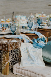 Coastal-chic seaside bridal dessert table with pastel shell-decor cake, cupcakes, blue goblets and nautical netting on a rustic wooden table with a tote bag