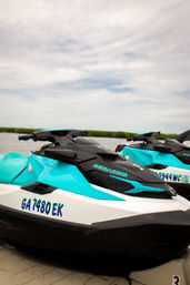 Two turquoise-and-white jet skis docked on a floating platform by coastal marsh under a cloudy sky