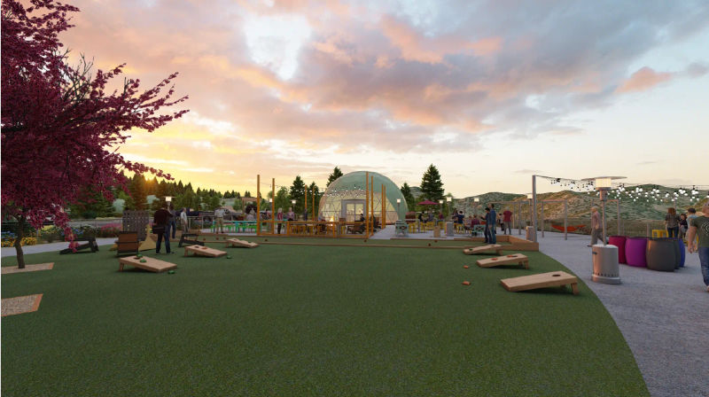 Sunset hilltop social lawn with cornhole boards, a glowing geodesic dome lounge, string lights and patio seating as people mingle against forested rolling hills.