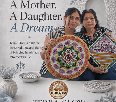 Mother and daughter artisans in a bright studio holding colorful handmade mandala and geometric wall art pieces, styled with decorative bowls and carved Indian-inspired backdrop — artisan home decor.