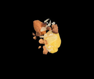 Close-up of a playful plated dessert: bright yellow mango-like puree with caramel-brown cookie crumbles and white coconut shavings on a black background.