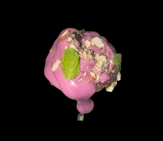 Bright pink-glazed dessert pop on a stick with chocolate base, crushed nuts and fresh mint leaves, isolated on black background