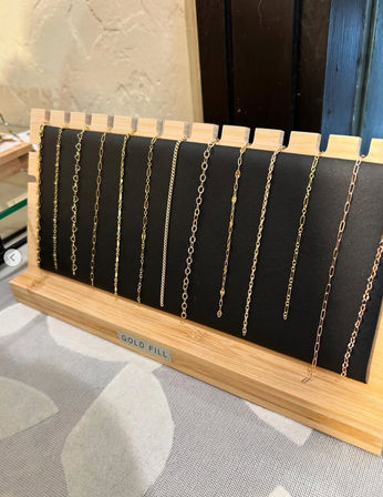 Delicate gold-filled chain necklaces displayed on a black leatherette panel with a light wood tabletop stand — boutique jewelry display