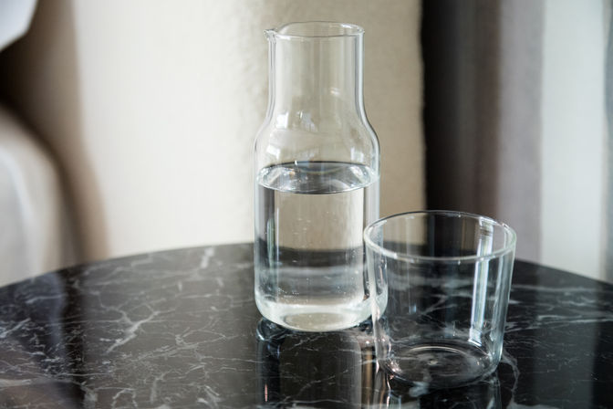 Sleek clear glass carafe half-filled with water next to an empty tumbler on a glossy black marble table, minimalist still-life.