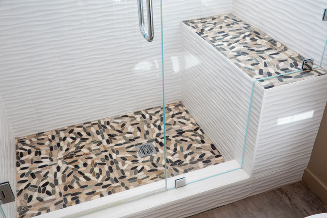 Glass-enclosed walk-in shower with pebble mosaic tile floor, built-in bench and white wavy textured wall tiles