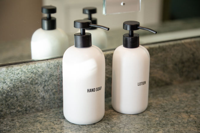 Two white pump dispensers labeled Hand Soap and Lotion on a granite bathroom countertop in front of a mirror, minimalist toiletry setup.