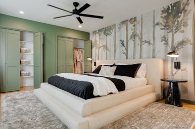 Cozy contemporary bedroom with low upholstered platform bed, black-and-white bedding, forest wall mural, sage green closet doors, black ceiling fan and marble bedside table on a textured area rug.