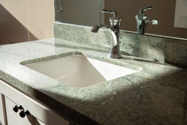 Sunlit bathroom vanity with green granite countertop, under-mount white sink and polished chrome single-handle faucet reflected in a mirror.