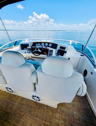 White boat helm with twin cushioned captain chairs, wooden steering wheel and instrument panel overlooking calm blue lake and sunny sky — ready for a relaxing cruise
