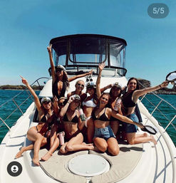 Group of friends in bikinis and captain hats partying on the bow of a white motor yacht in sunny blue coastal waters with shoreline in the background