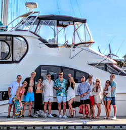Dozen friends posing on a marina dock in summer outfits in front of a luxury white yacht on a sunny coastal day, upbeat vacation vibe.