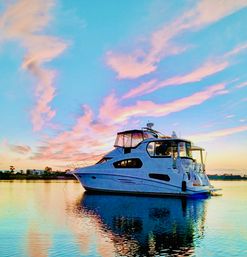 Luxury white motor yacht anchored in a calm coastal harbor at sunset with pastel pink and blue clouds reflected on glassy water