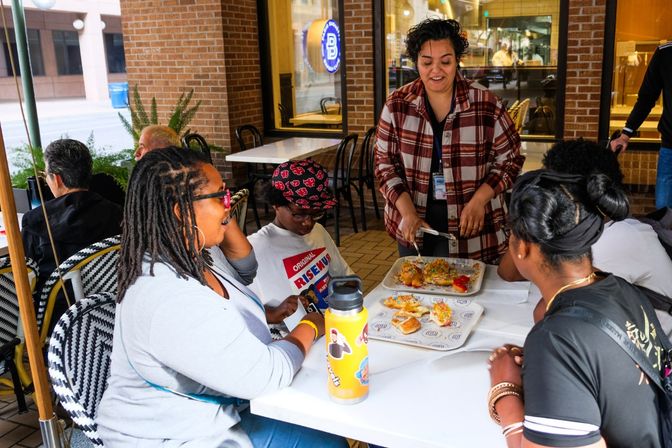 Group of friends seated at a downtown outdoor cafe patio as a server brings trays of colorful, sprinkled pastries