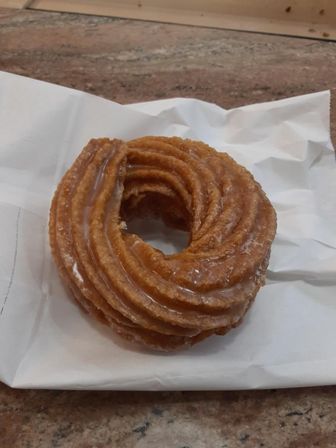 Glazed ridged cruller doughnut on a white paper wrapper sitting on a stone countertop — bakery-style breakfast pastry.