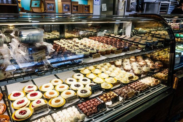 Glass bakery display case in a pastry shop filled with rows of frosted cupcakes, mini cheesecakes, fruit tarts and chocolate truffles