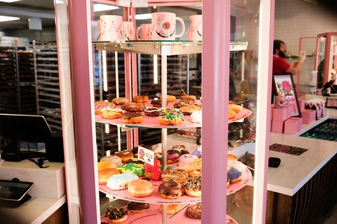 Colorful assorted gourmet donuts on a pink rotating glass display case at a trendy indoor donut shop counter