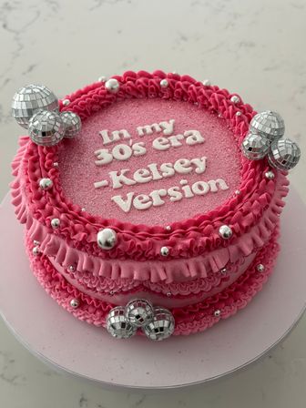 Pink birthday cake with ruffled buttercream, white piped message referencing being in your 30s, glittered top, silver dragees and small disco-ball cake toppers