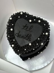 Heart-shaped black buttercream cake with ruffled border, scattered white edible pearls and "til death" piping — gothic-style wedding or Halloween dessert.