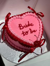 Heart-shaped pink frosted cake with red ribbon bows, cherry and red icing script reading 'Bride to be' — bridal shower / bachelorette party dessert